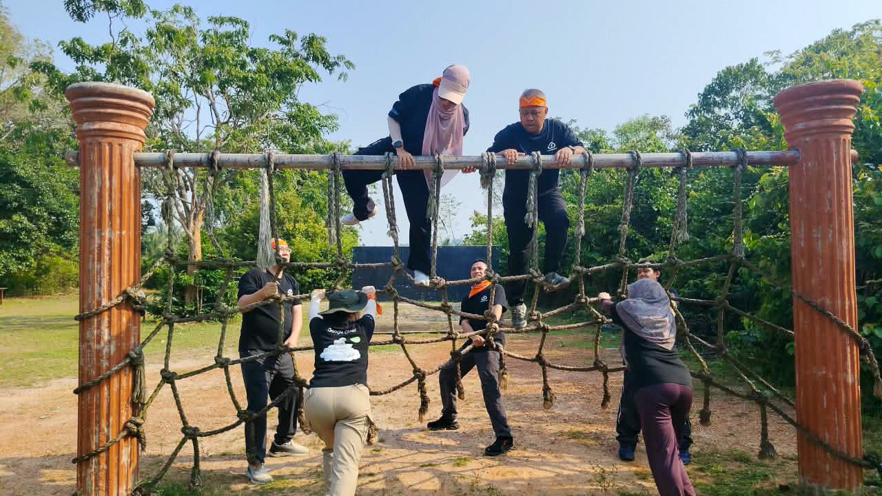 Colleagues helping each other across a rope obstacle course